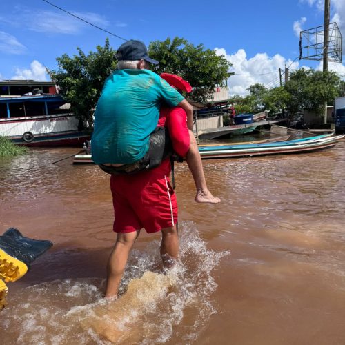 Bombeiro carrega idoso nas costas durante resgate em área alagada no Rio Juruá